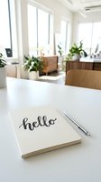 Notebook with hello lettering and silver pen on white desk in bright modern office with plants and wooden furniture.