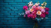 Vibrant bouquet with pink orchids and peach roses against turquoise brick wall background, featuring eucalyptus leaves and mixed florals in romantic arrangement.