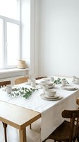 Minimalist dining table setup with white ceramic tableware, linen tablecloth, eucalyptus greenery, and wooden chairs near bright window with natural light for home decor and lifestyle content.
