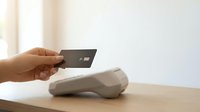 Hand holding black credit card over contactless payment terminal on wooden table for secure financial transaction.