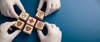 Healthcare professional hands in white gloves arranging wooden blocks with medical icons including stethoscope, heart, and cross symbols on blue background for hospital or clinic branding.
