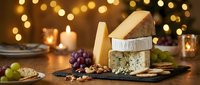 Festive cheese board with brie, blue cheese, and aged cheddar, served with grapes, crackers, and nuts on a slate platter with warm holiday lights.