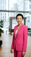 Confident Asian woman in vibrant pink business suit standing in modern office lobby with floor-to-ceiling windows overlooking cityscape. Corporate portrait.