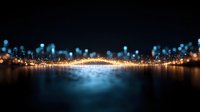 Glowing city lights reflected on dark water surface with bokeh effect and illuminated bridge creating magical nighttime urban landscape atmosphere.