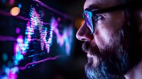 Side profile of bearded programmer in glasses looking at glowing computer code display with purple and blue digital data visualization reflections.