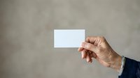 Mature man with light skin tone holding blank white business card against neutral gray background for corporate branding and professional mockup purposes.