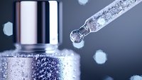 Macro shot of glass dropper with liquid drops and silver bottle cap on dark background with bokeh effect and water droplets creating artistic composition.
