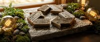 Dark chocolate pieces arranged on rustic slate board with moss, nuts and warm Edison bulb lighting creating cozy artisanal confectionery display atmosphere.