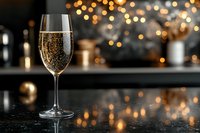 Elegant champagne flute filled with sparkling wine on marble counter with warm golden bokeh lights creating luxurious celebration atmosphere for holidays and events.