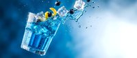 Fresh blue cocktail with ice cubes splashing in glass against gradient background for beverage advertising and summer drink promotions.