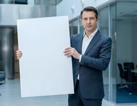 Professional businessman in suit holding blank white poster in modern office environment for corporate presentations and marketing campaigns.