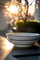 Empty ceramic bowls with gold rim catching morning sunlight, bokeh effect in background creates cozy atmosphere. Minimalist table setting for breakfast or dining.