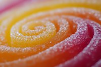 Colorful spiral candy with sugar crystals in vibrant rainbow hues of pink, orange and yellow creating sweet confectionery texture for dessert designs.