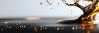 Dramatic liquid splash with golden amber drops and dark background creating dynamic motion effect with bokeh lights and reflective surface.