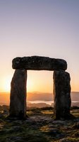 Ancient stone monument framing golden sunrise over misty valley landscape. Megalithic gateway structure silhouetted against dawn sky with mountains and water visible through opening.