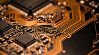 Close-up macro view of orange printed circuit board with intricate copper traces, electronic components, and microchips for technology projects.