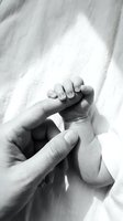 Tender moment of parent holding newborn baby hand in black and white monochrome photography capturing love bond between mother father and infant child.