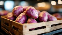 Fresh purple potatoes in rustic wooden crate with soft bokeh background, close up view of organic farm produce showing natural texture and color.