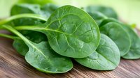 Fresh raw spinach leaves with water drops on wooden cutting board, macro view showing detailed leaf texture and vibrant green color. Natural food photography.