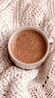 Frothy hot chocolate in white ceramic cup placed on cozy knitted sweater background, creating warm and comforting winter mood with rich cocoa bubbles.