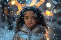 Young African American girl in silver winter jacket smiling at camera during snowfall with bokeh lights creating magical winter atmosphere in background.