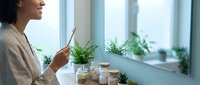 Young African American woman enjoying herbal tea in bright modern kitchen with fresh plants on windowsill creating peaceful morning wellness routine.
