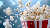Fresh popcorn overflowing from red striped container against blue bokeh background, flying kernels create dynamic composition for food and entertainment concepts.