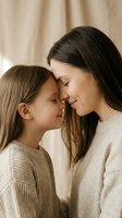 Caucasian mother and daughter touching foreheads, sharing a tender moment in cozy knit sweaters against a warm beige background.