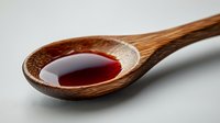 Wooden spoon filled with dark red liquid medicine or syrup on white background for health and wellness concepts.