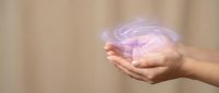 Hands cupping glowing purple energy swirl with magical light effects against soft beige background for wellness and spiritual healing concepts.