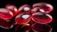 Red transparent krill oil capsules or omega-3 supplements on black reflective surface with soft focus background showing nutritional supplements for health benefits.
