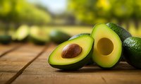 Fresh ripe avocado cut in half showing pit and creamy flesh on rustic wooden surface with soft bokeh background, natural food photography styling.