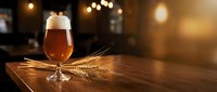 Craft beer glass with foam on wooden table with wheat stalks in warm pub atmosphere with bokeh lights creating cozy ambiance for brewery marketing materials.