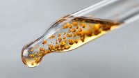 Macro shot of golden liquid with air bubbles in glass dropper against light background, showing viscosity and transparency in medical or cosmetic context.