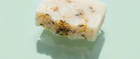Handmade natural soap bar with dried herbs and flowers on mint green background for skincare and wellness products.