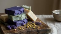 Handmade natural soap bars in purple and beige colors stacked on rustic wooden cutting board with dried lavender flowers for spa and skincare routine.