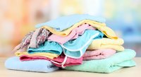 Colorful pile of folded baby clothes and towels in soft pastel colors on white surface with blurred background for nursery and childcare concepts.