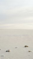 Serene beach landscape with smooth sand ripples and scattered stones under soft overcast sky for peaceful coastal backgrounds.