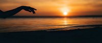 Hand reaching toward golden sunset over calm ocean waves creating peaceful moment of connection with nature and tranquil seascape for meditation concepts.