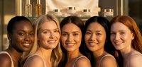 Group of five diverse young women smiling together in luxury spa setting with golden skincare products, representing friendship and wellness lifestyle.