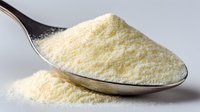 Creamy yellow powdered milk on silver spoon against neutral background, essential ingredient for baking and cooking recipes.