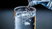 Clear water pouring from bottle into drinking glass with dynamic splash and bubbles against dark background, dramatic lighting highlights liquid motion and transparency.