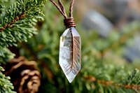 Crystal quartz pendant with copper wire wrap and feather detail against natural green foliage and pine cone background, bohemian jewelry photography.