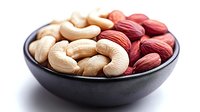 Raw cashews and red almonds in black ceramic bowl on white background, healthy nuts and seeds mix for snacking and cooking, macro food photography.