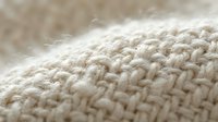 Close-up macro shot of natural beige wool yarn texture showing detailed knitted fabric fibers and soft organic cotton material for cozy home decor projects.