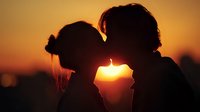 Romantic couple silhouette kissing at golden sunset, intimate moment between man and woman against warm orange sky backdrop for love and relationship concepts.