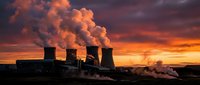 Nuclear power plant cooling towers emitting steam against dramatic orange sunset sky creating industrial energy landscape for environmental concepts.
