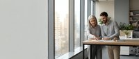Professional mature couple collaborating on business documents in modern office workspace with large windows and natural lighting for corporate teamwork.
