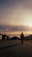 Silhouette of man walking down suburban street at sunset with warm golden light and lens flares creating atmospheric mood in residential neighborhood.