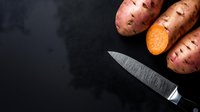 Fresh raw sweet potatoes and sharp kitchen knife on dark background with copy space for text, overhead view of organic root vegetables.